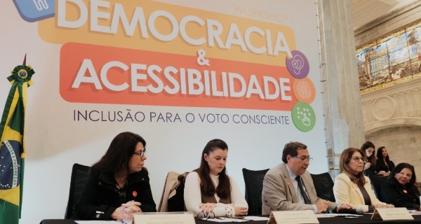 TRE-RJ firma compromisso em se tornar 100% acessível até 2027 A mesa de abertura do evento com um painel ao fundo "Workshop Democracia & Acessibilidade", com...