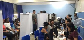 Local do atendimento itinerante em Itaguaí, onde eleitoras(es) estão sentadas sendo atendidas pe...