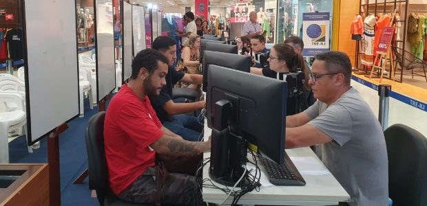 TRE-RJ inicia atendimento itinerante em São Gonçalo A imagem mostra um balcão de atendimento, onde há uma fila de computadores, os guichês de atendi...