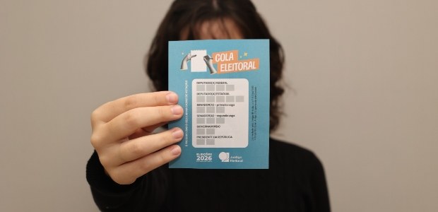 Mulher segura uma cartilha de “Cola Eleitoral” em frente ao rosto, destacando a orientação para ...