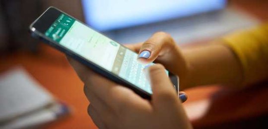 Uma pessoa segura um smartphone com as duas mãos e digita na tela, que exibe uma interface de co...