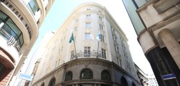 Descrição da imagem: A imagem mostra um edifício de arquitetura clássica, de vários andares, com...