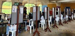 A foto mostra os guichês de atendimento montados em um colégio. O atendimento acontece em um loc...