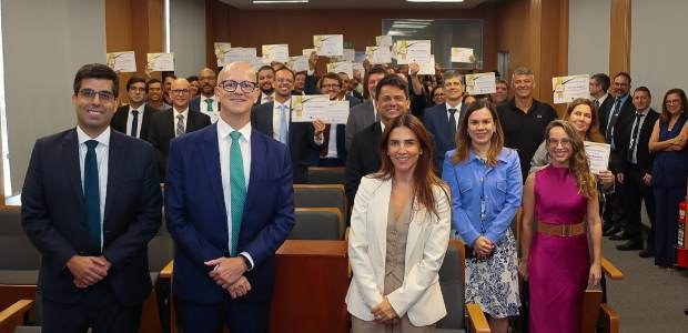 TRE-RJ premia cartórios por desempenho na gestão processual Magistrados(as) e servidoras(es) estão de pé, sorrindo, posando para a foto. Muitos estão mostra...