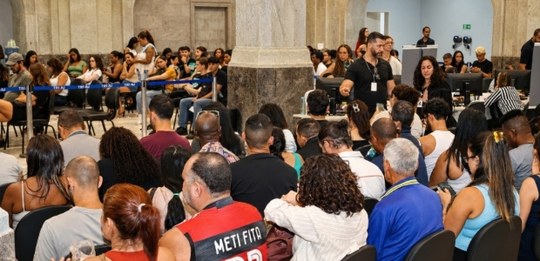 Grande público sentado em filas dentro do Palácio da Democracia, aguardando atendimento.