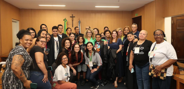 O grupo de pessoas posa para uma foto coletiva dentro do plenário. Estão presentes adolescentes,...
