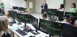 A imagem mostra um ambiente de sala de aula com várias estações de trabalho de computador. Cada ...