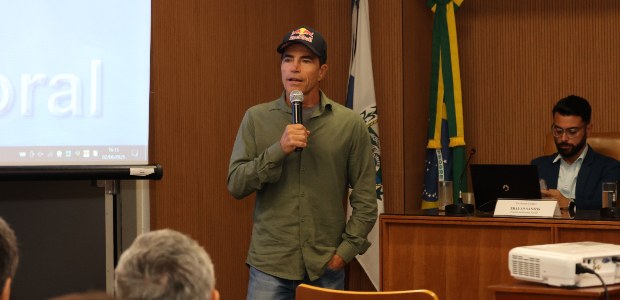 TRE-RJ: Surfista bicampeão mundial de ondas gigantes abre 16ª Semana Ambiental O surfista está em pé, falando ao microfone. Ele veste uma camisa verde de manga comprida, calça...