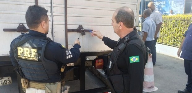 TRE-RJ tem o apoio da PRF e da PMERJ para fazer o transporte de urnas Foto de dois agentes de segurança lacrando um dos caminhões de transporte. eles vestem roupas pr...