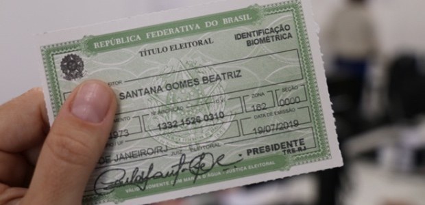 TRE-RJ Título Mão segura um título eleitoral, onde lê-se "Identificação Biométrica"