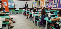 Numa sala de aula, em primeiro plano, sentados, estudantes assistem à palestra do juiz eleitoral...