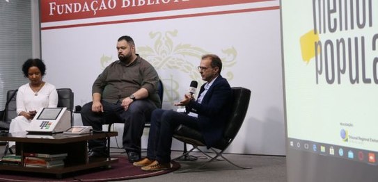 Três pessoas estão sentadas em um semicírculo; da esquerda para a direita, Ana Flávia Magalhães ...
