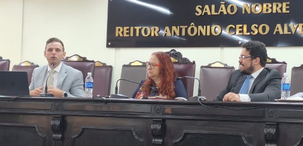 Foto dos participantes sentados à mesa. À esquerda, o magistrado Bruno Bodart, um homem branco, ...