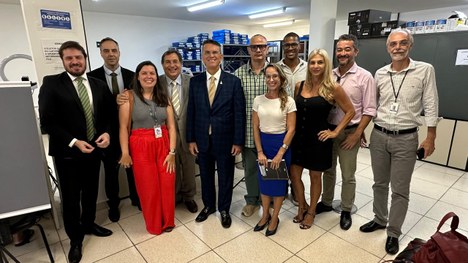 Magistrados e servidoras(es) estão, lado a lado, de pé e sorrindo